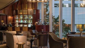 A modern bar area with a large chandelier, seating arrangements, and a view of the cityscape through large windows. - Conrad Hong Kong (Hong Kong)