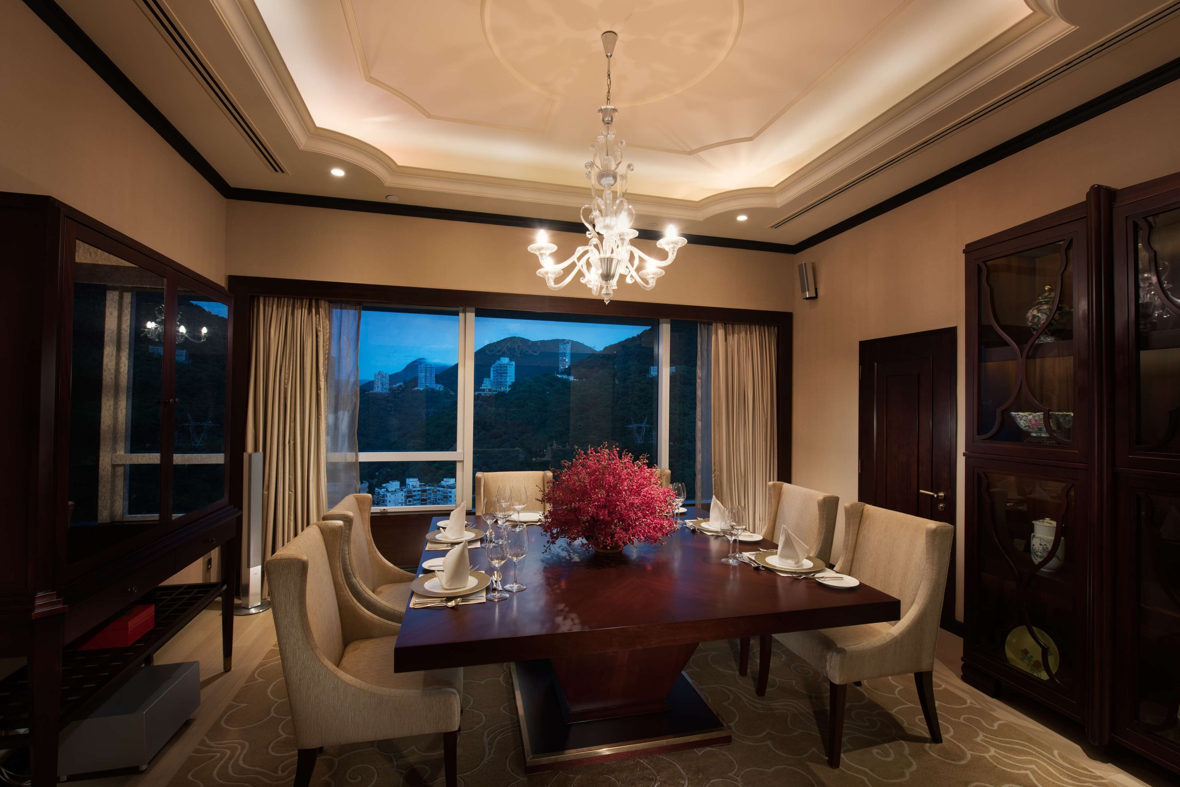 Une salle à manger avec une grande table dressée pour six personnes, un lustre et une vue sur les montagnes par les fenêtres.