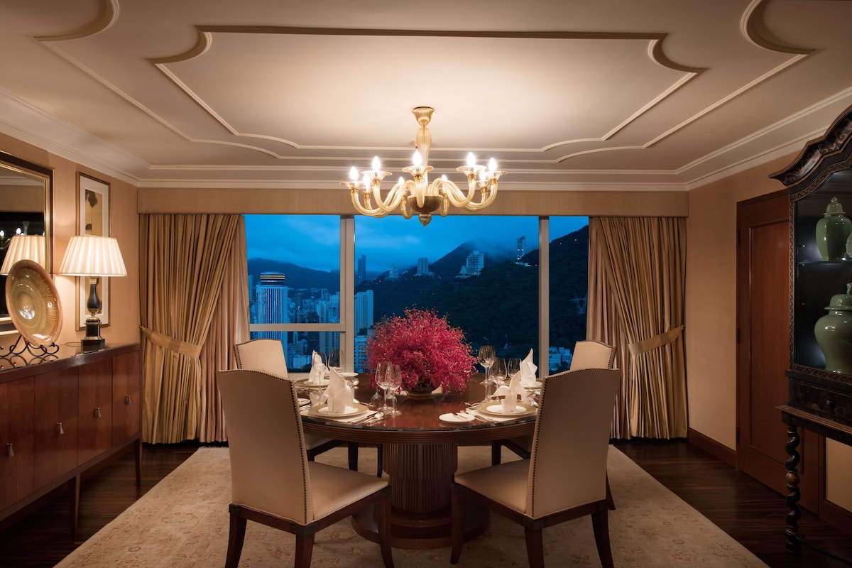 Una sala da pranzo con un lampadario, un tavolo apparecchiato per quattro persone e vista sulla città al crepuscolo.