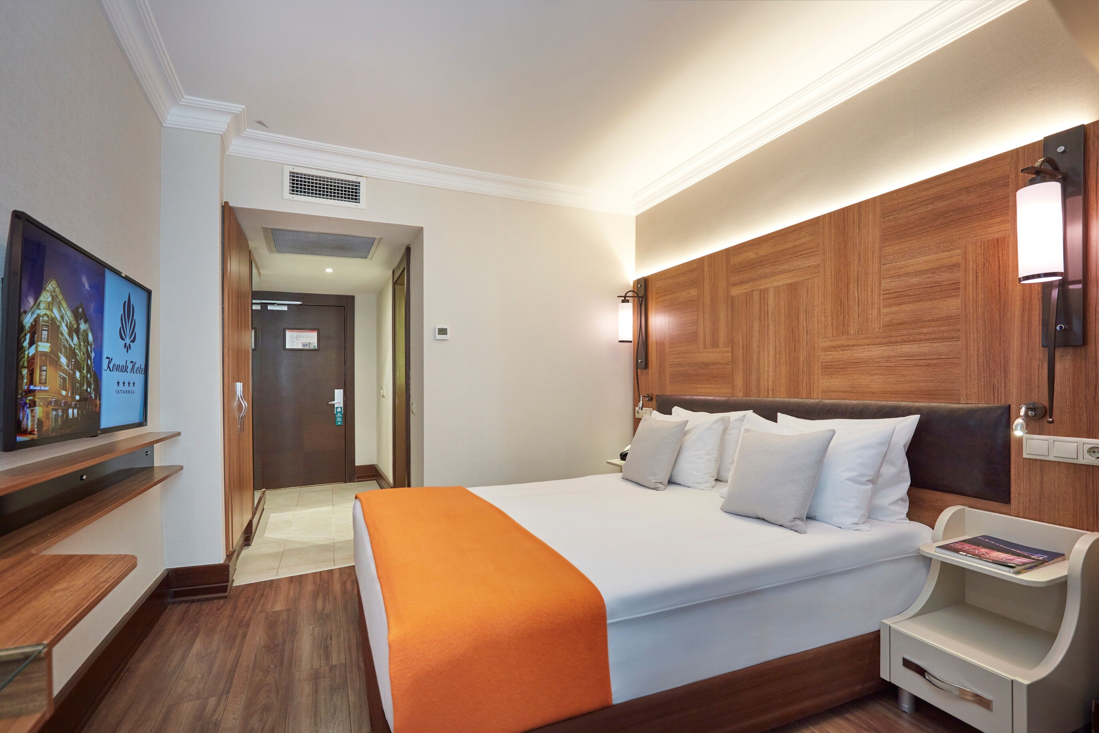Une chambre d’hôtel avec un grand lit, une table de chevet, un téléviseur et une tête de lit en bois.