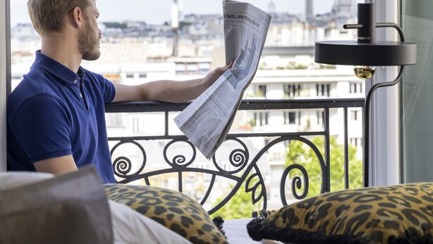 Una persona leyendo un periódico en un balcón con vistas a la ciudad.