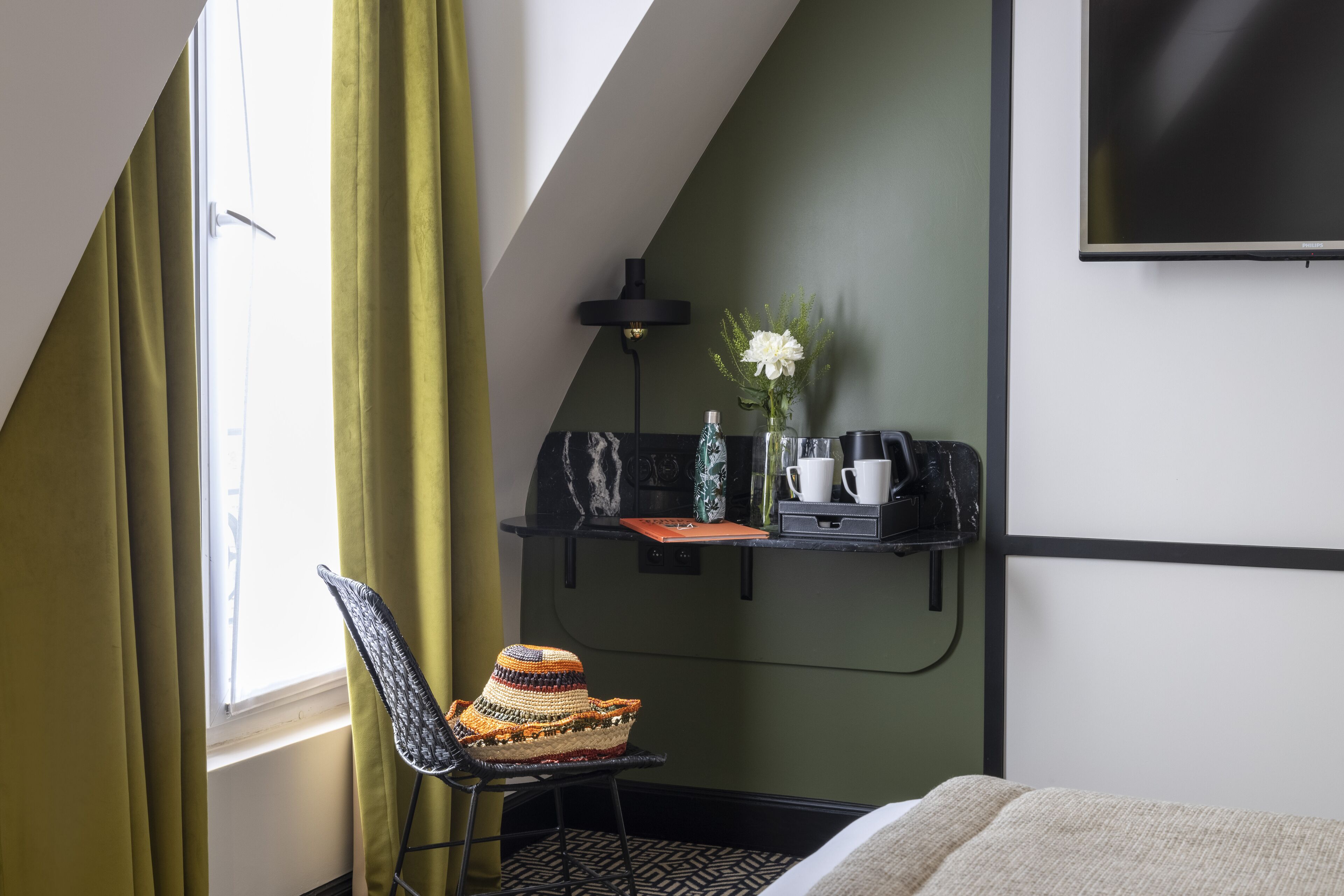 A hotel room with a sloped ceiling, a desk with a lamp, a chair, and a bed.