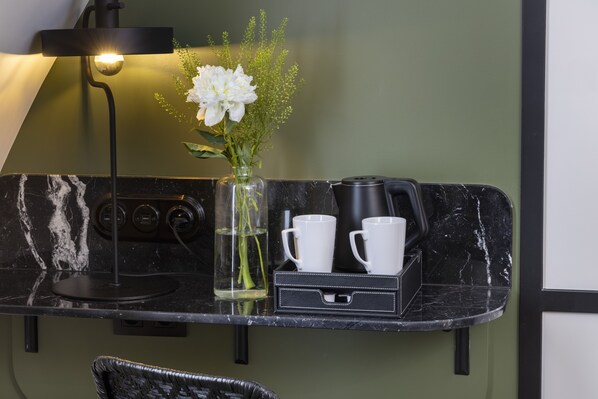 A kitchen counter with a coffee maker, two white cups, a vase with flowers, and a lamp. - Grand Hôtel Chicago (Paris)