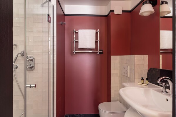 Un baño moderno con cabina de ducha de vidrio, un lavamanos blanco y una pared de acento roja.