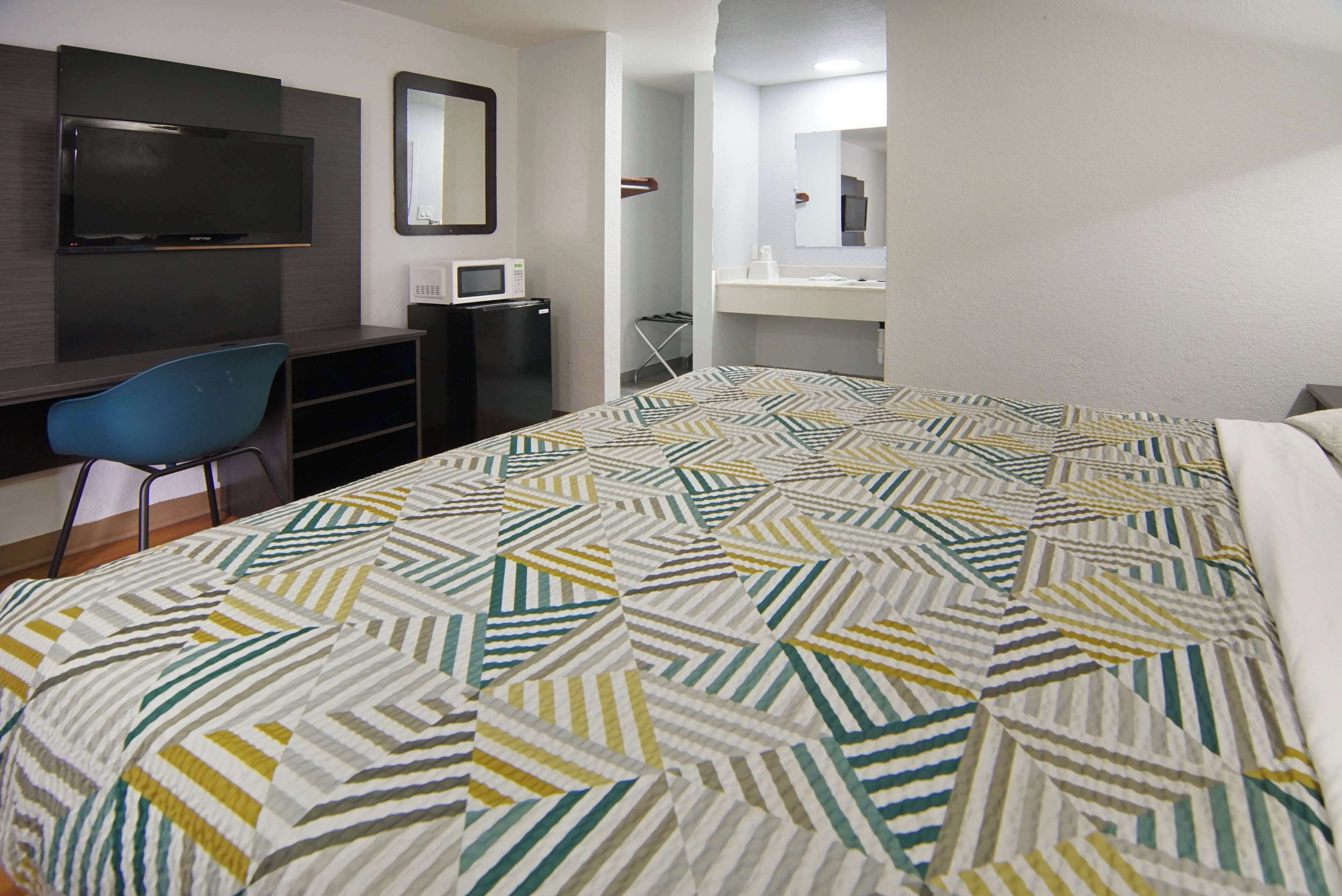 Habitación de hotel con cama, escritorio con silla, televisor, microondas y baño con espejo.