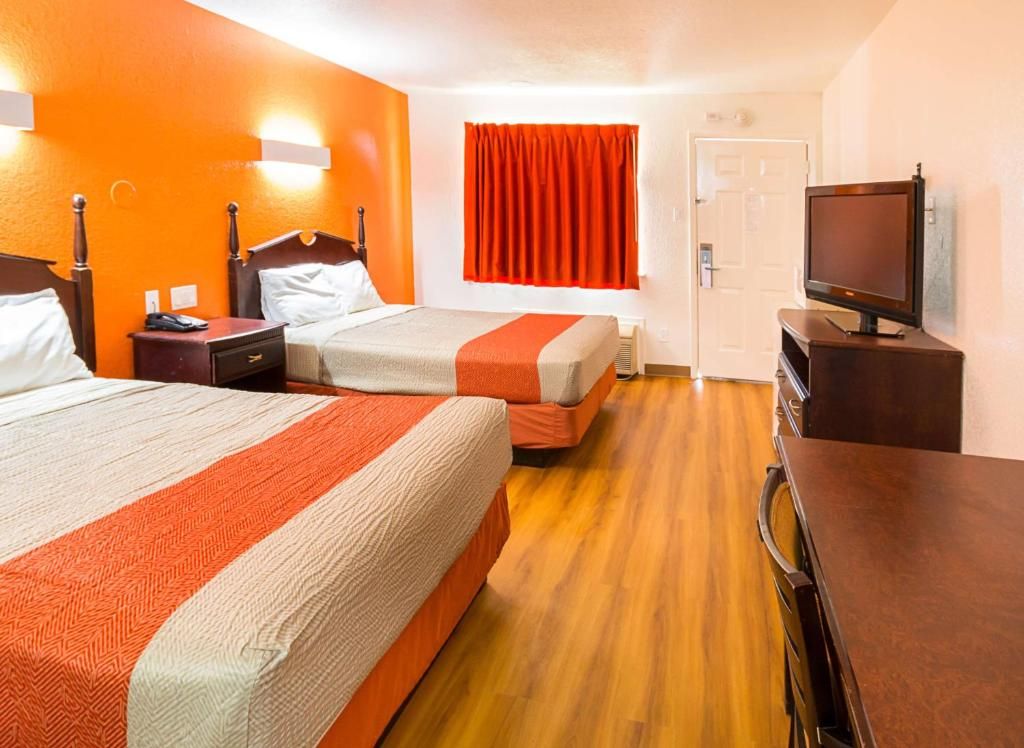 Quarto de hotel com duas camas, uma televisão e uma porta.