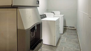 Un lavadero con lavadora y secadora de acero inoxidable, un dispensador de agua y piso de baldosas.