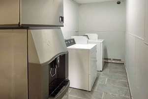Un lavadero con lavadora y secadora de acero inoxidable, un dispensador de agua y piso de baldosas.