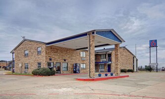 Un motel con fachada de ladrillo, un área de estacionamiento techada y un letrero que indica el número 6.