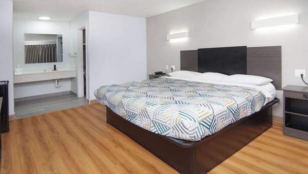 Una habitación de hotel moderna con una cama grande, un escritorio empotrado, un tocador con espejo y una zona de ducha.