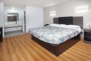 Una habitación de hotel moderna con una cama grande, un escritorio empotrado, un tocador con espejo y una zona de ducha.