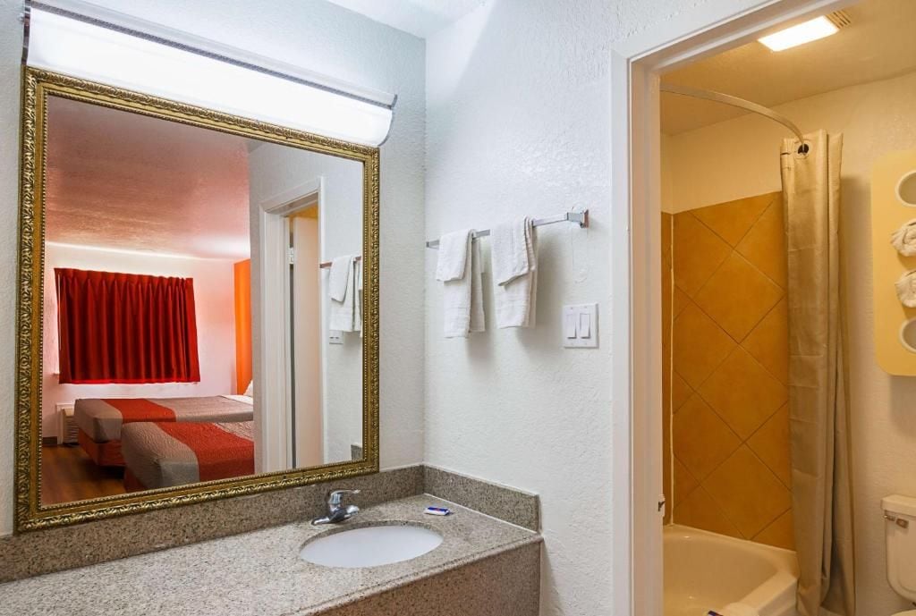 A bathroom with a large mirror, a sink, a shower, and a toilet.