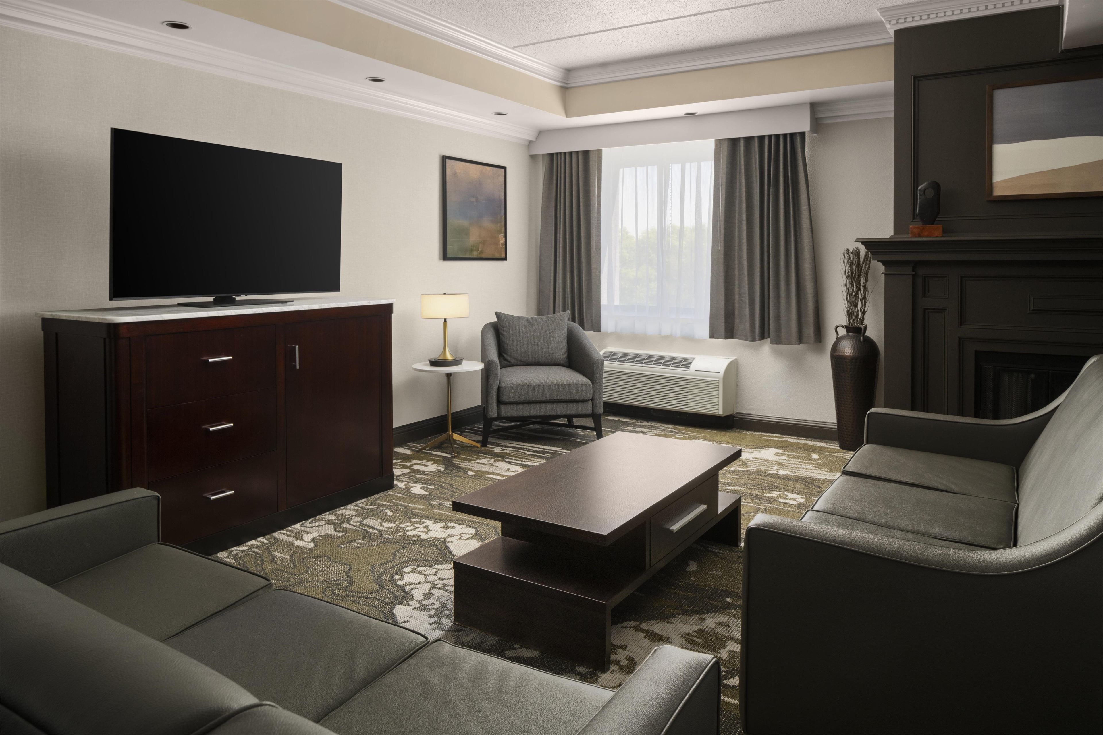 Ein Hotelzimmer mit Flachbildfernseher, einer Couch, einem Sessel, einem Couchtisch, einer Lampe und einem Kamin.