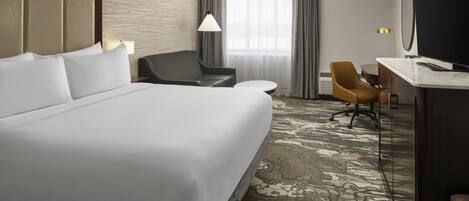 Quarto de hotel com uma cama grande, uma escrivaninha com cadeira, televisão e janela com cortinas.