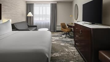 A hotel room with a large bed, a desk, a chair, a television, and a carpeted floor.