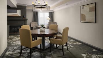 Une salle à manger d’hôtel avec une table ronde, quatre chaises, un lustre, une cheminée et un grand tableau abstrait accroché au mur.