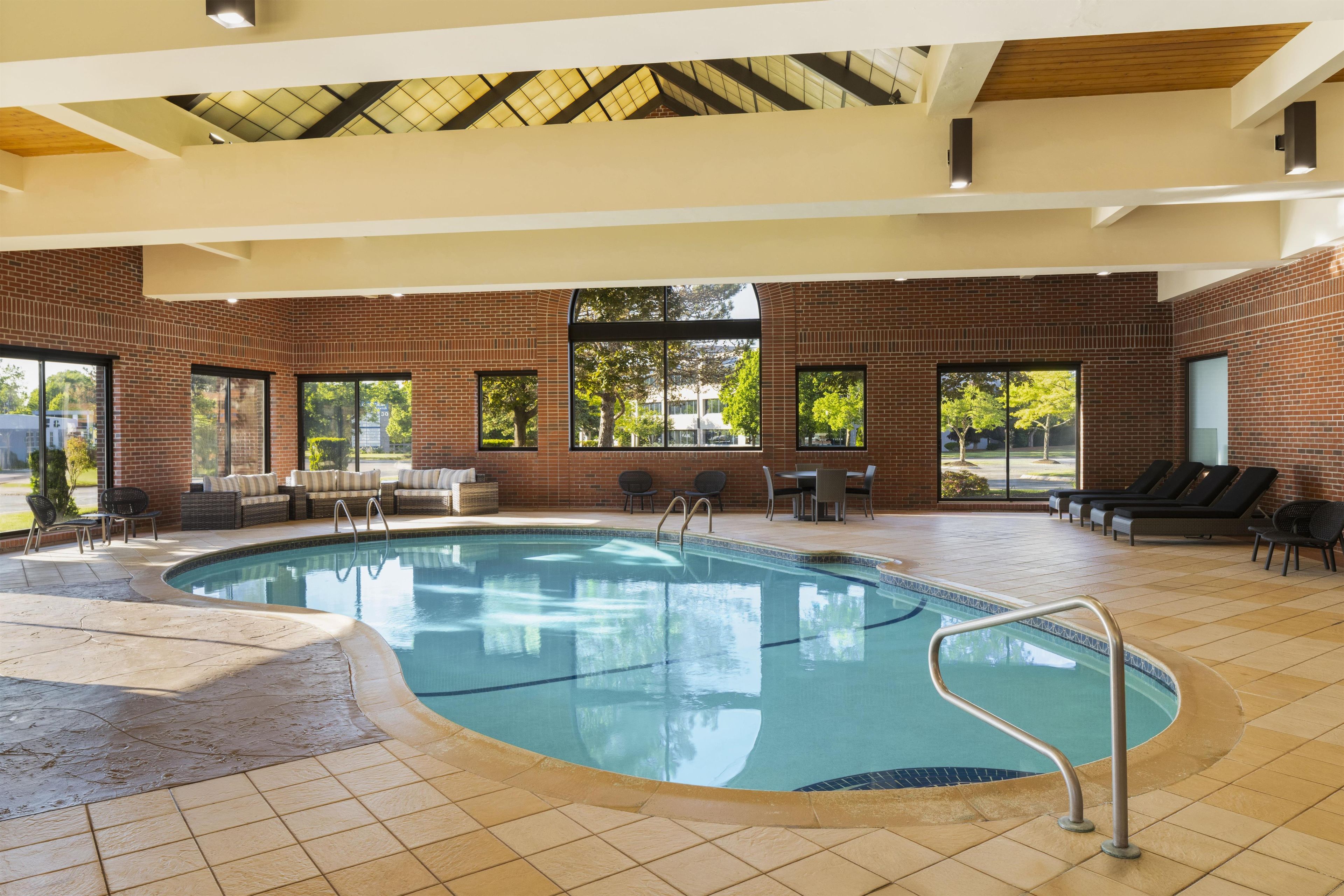 An indoor swimming pool with a tiled floor, surrounded by seating areas and large windows.