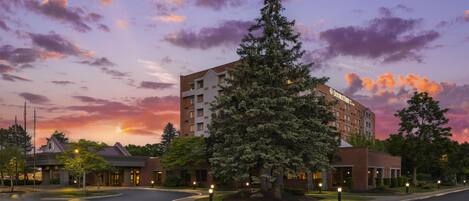 A hotel with a modern design, featuring a prominent tree in the foreground and a clear view of the sky.