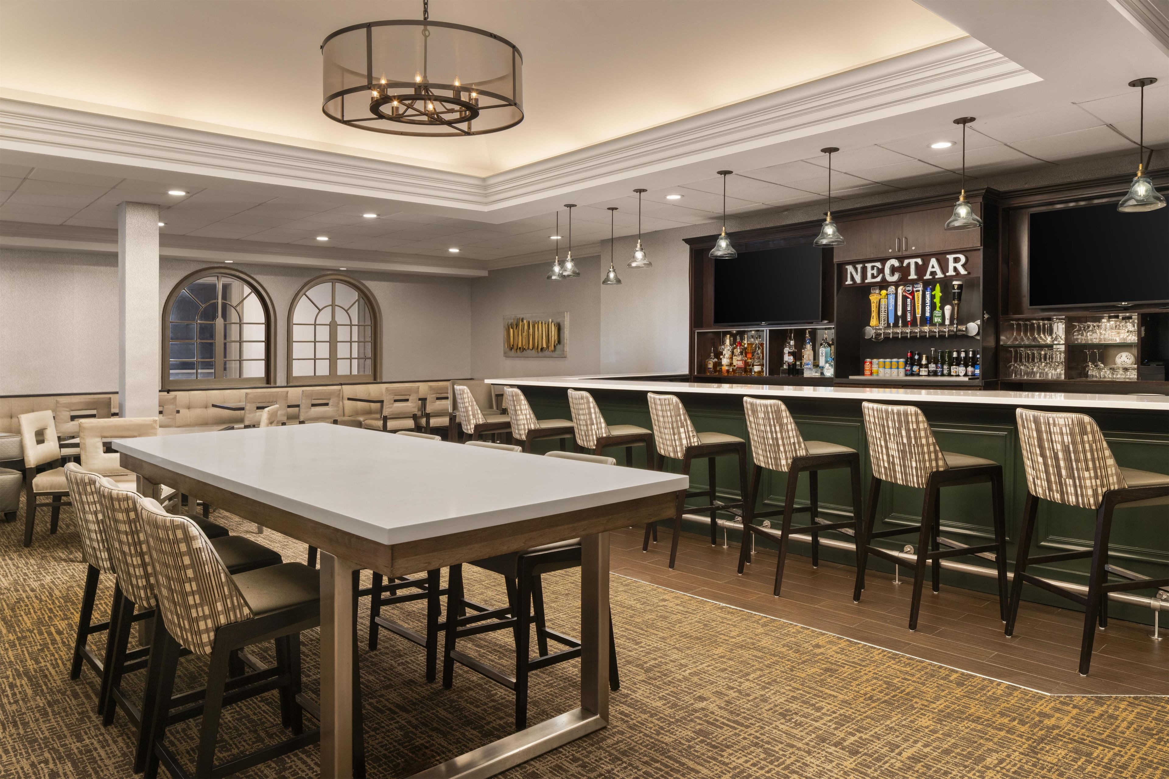 A bar area with a long counter, multiple bar stools, and a wall-mounted liquor dispenser labeled 'NECTAR'.