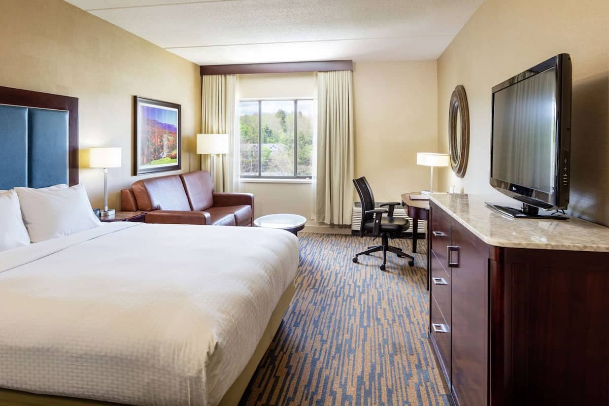 A hotel room with a large bed, a desk with a television, a chair, and a window with curtains.