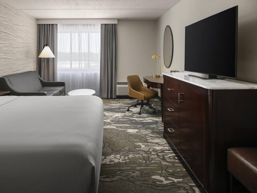 A hotel room with a large bed, a desk, a chair, a television, and a carpeted floor.