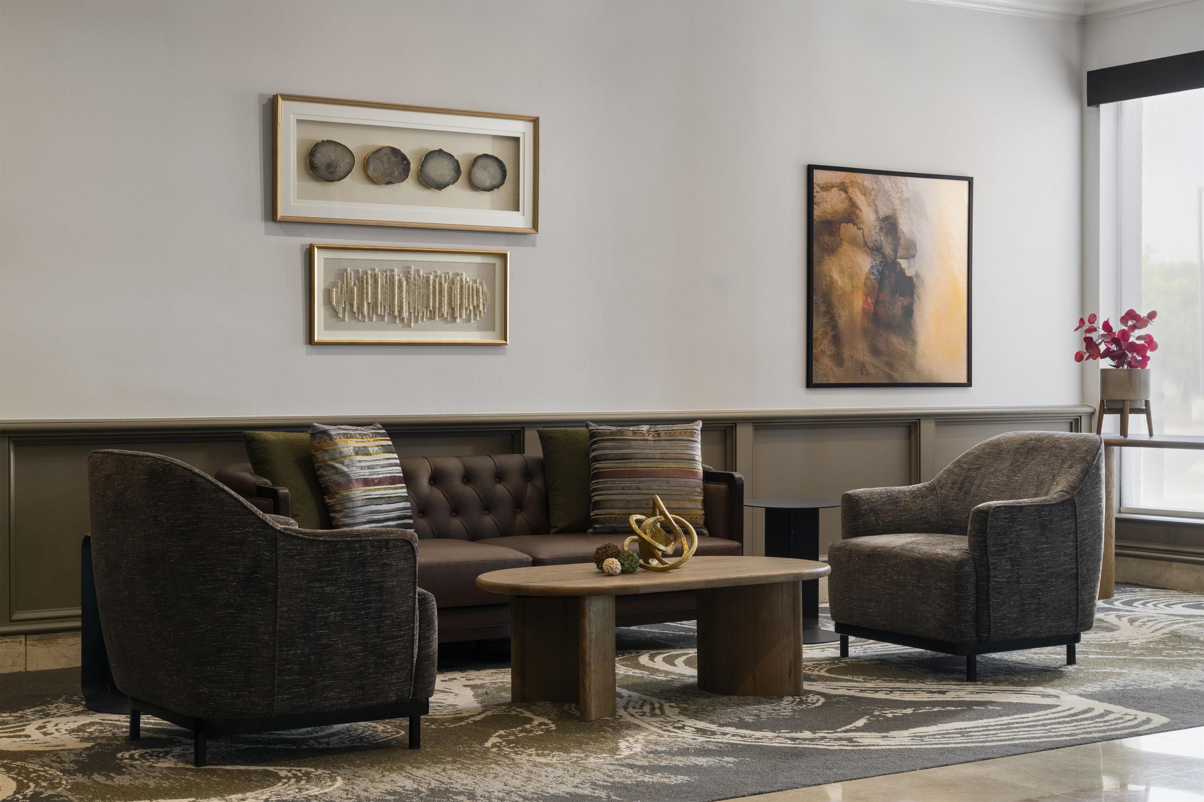 Un salon moderne avec un canapé d’angle, deux fauteuils, une table basse et des œuvres d’art accrochées aux murs.