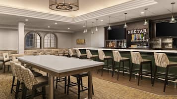 A bar area with a long counter, multiple bar stools, and a wall-mounted liquor dispenser labeled 'NECTAR'.