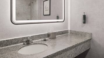 A bathroom with a granite countertop, a sink, a mirror, and a framed picture on the wall.