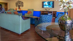 A lobby with a sofa, chairs, a glass table, a vase with flowers, and a TV on the wall.
