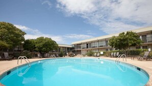 A swimming pool surrounded by lounge chairs and a building with multiple balconies.