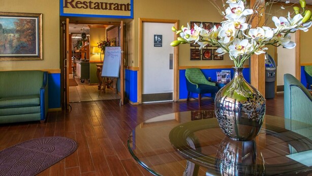 A hotel lobby with a glass table in the center, a vase of flowers, a green sofa, and a sign for the restaurant.