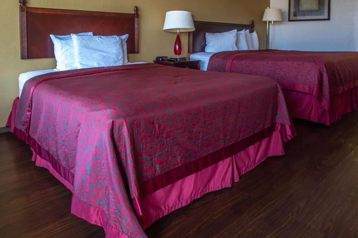 A hotel room with two beds, each with a red patterned bedspread, wooden headboards, and white pillows.