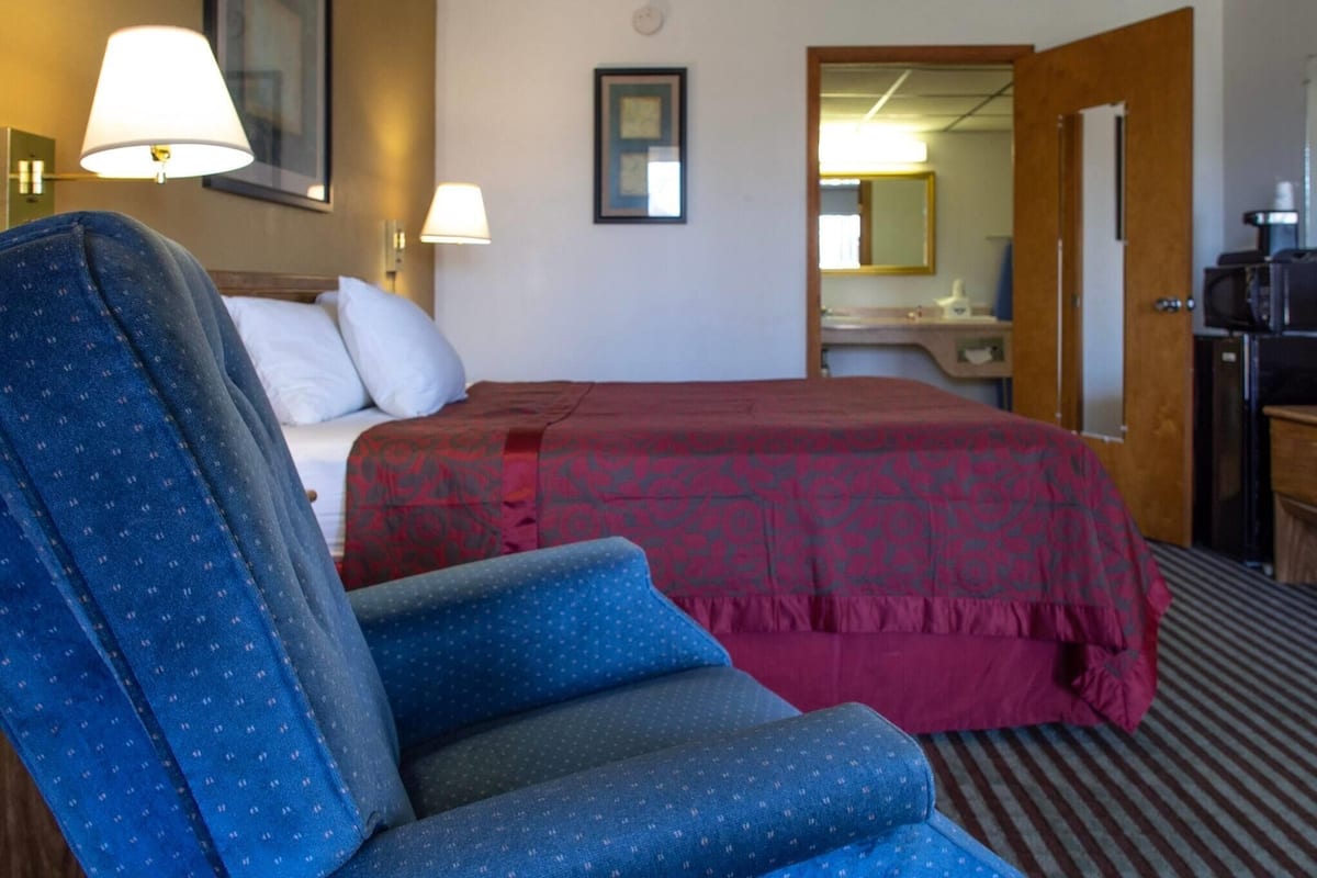A hotel room with a bed, a desk, a chair, and a mirror.