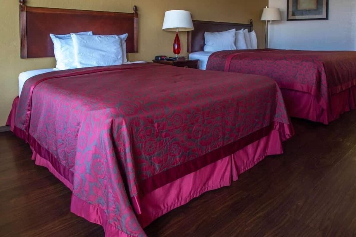 A hotel room with two beds, a wooden headboard, a nightstand, and a lamp.