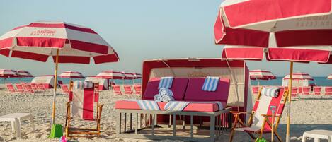 A beach with rows of red and white striped umbrellas, beach chairs, and a lounge area with a striped blanket.