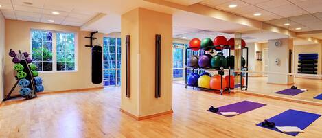Een ruime fitnessruimte met houten vloeren, trainingsapparatuur en grote ramen.