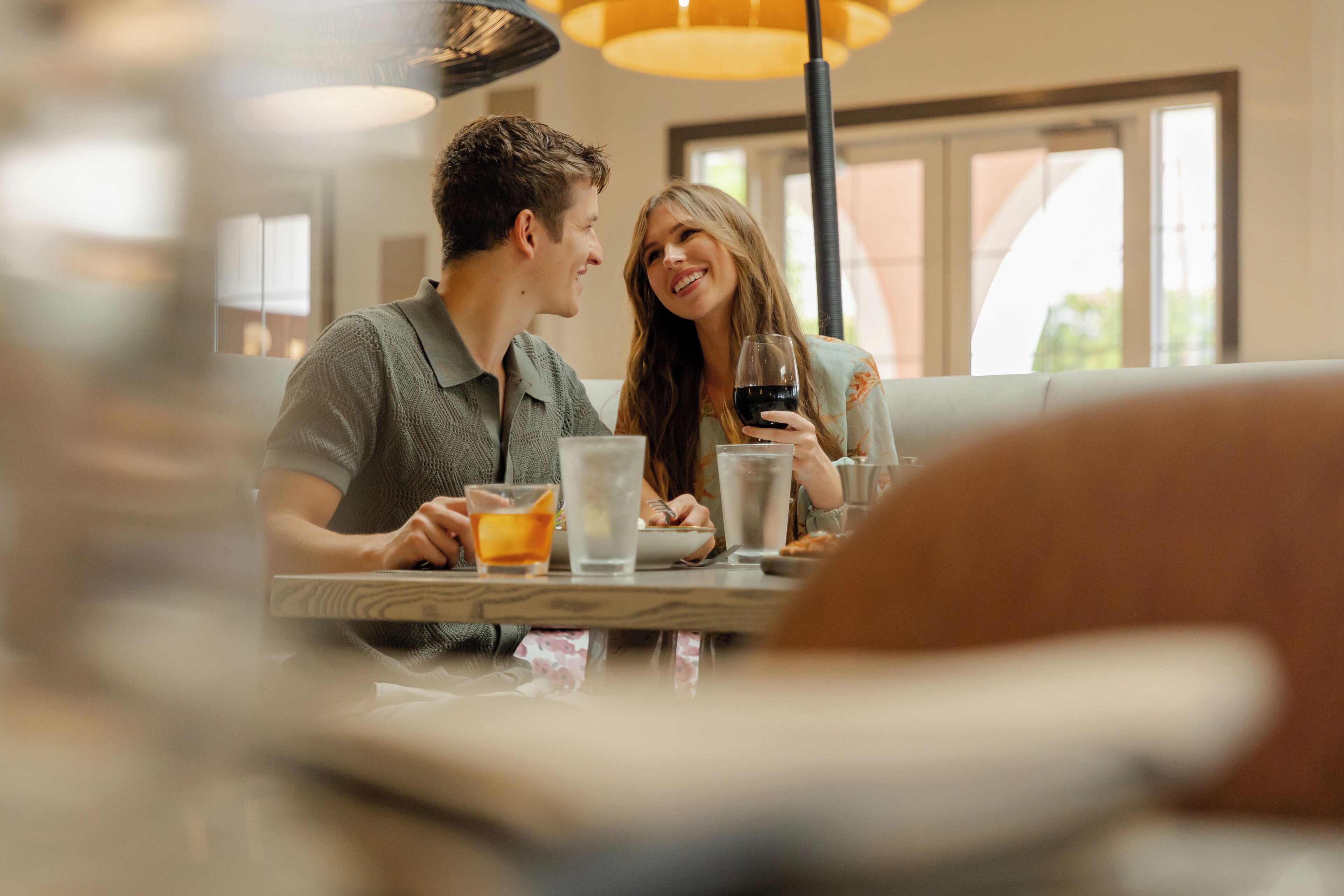 Un couple est assis à une table dans un restaurant, près d’une fenêtre donnant sur l’extérieur.