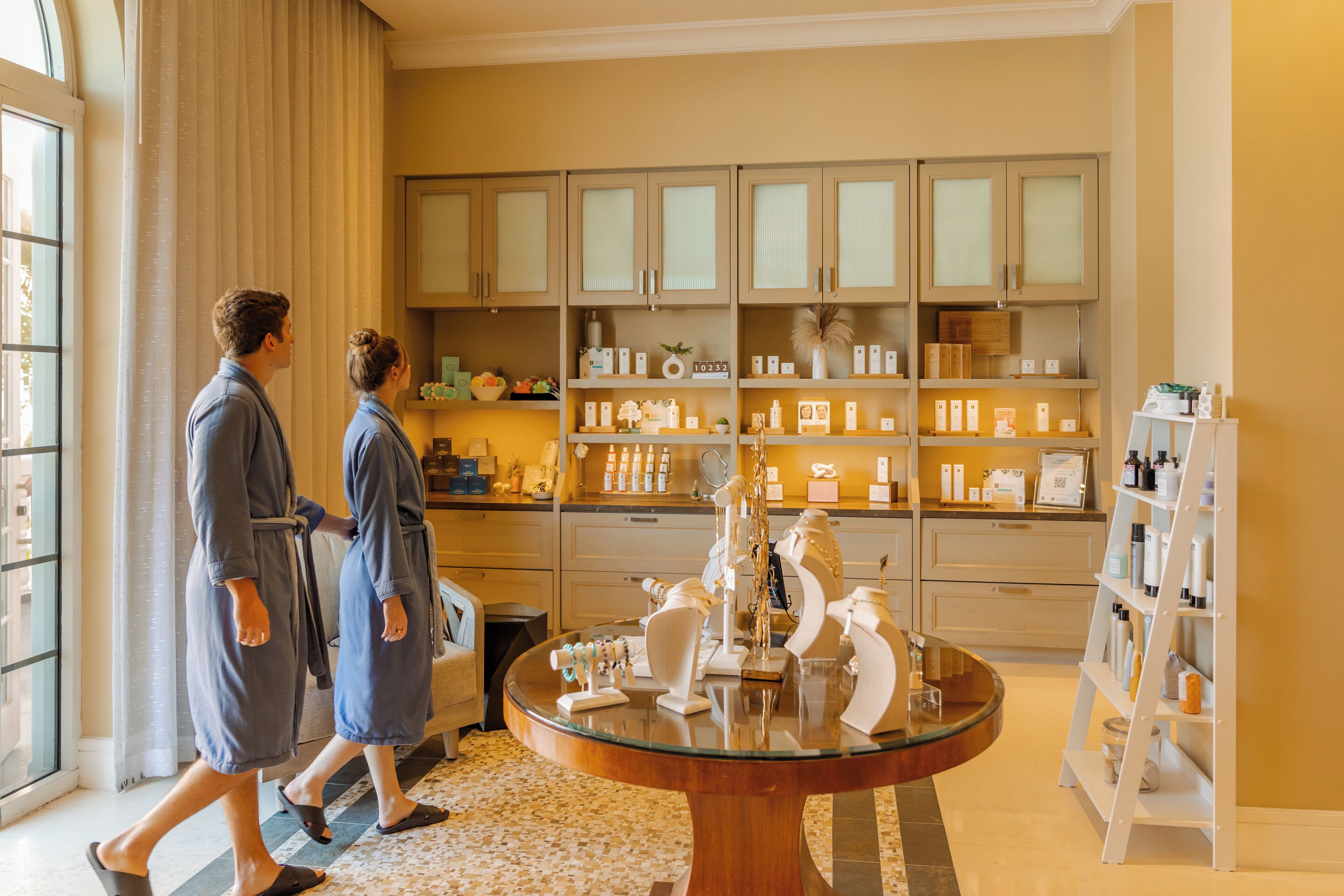 A hotel lobby with a large glass table, beige walls, and a variety of toiletries on shelves.
