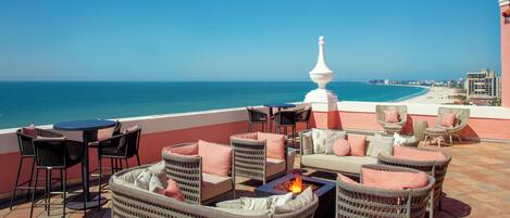 Una terraza con mobiliario de mimbre, un hogar y vistas al océano.
