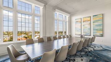 A conference room with a long table and chairs, large windows, and abstract paintings on the wall.