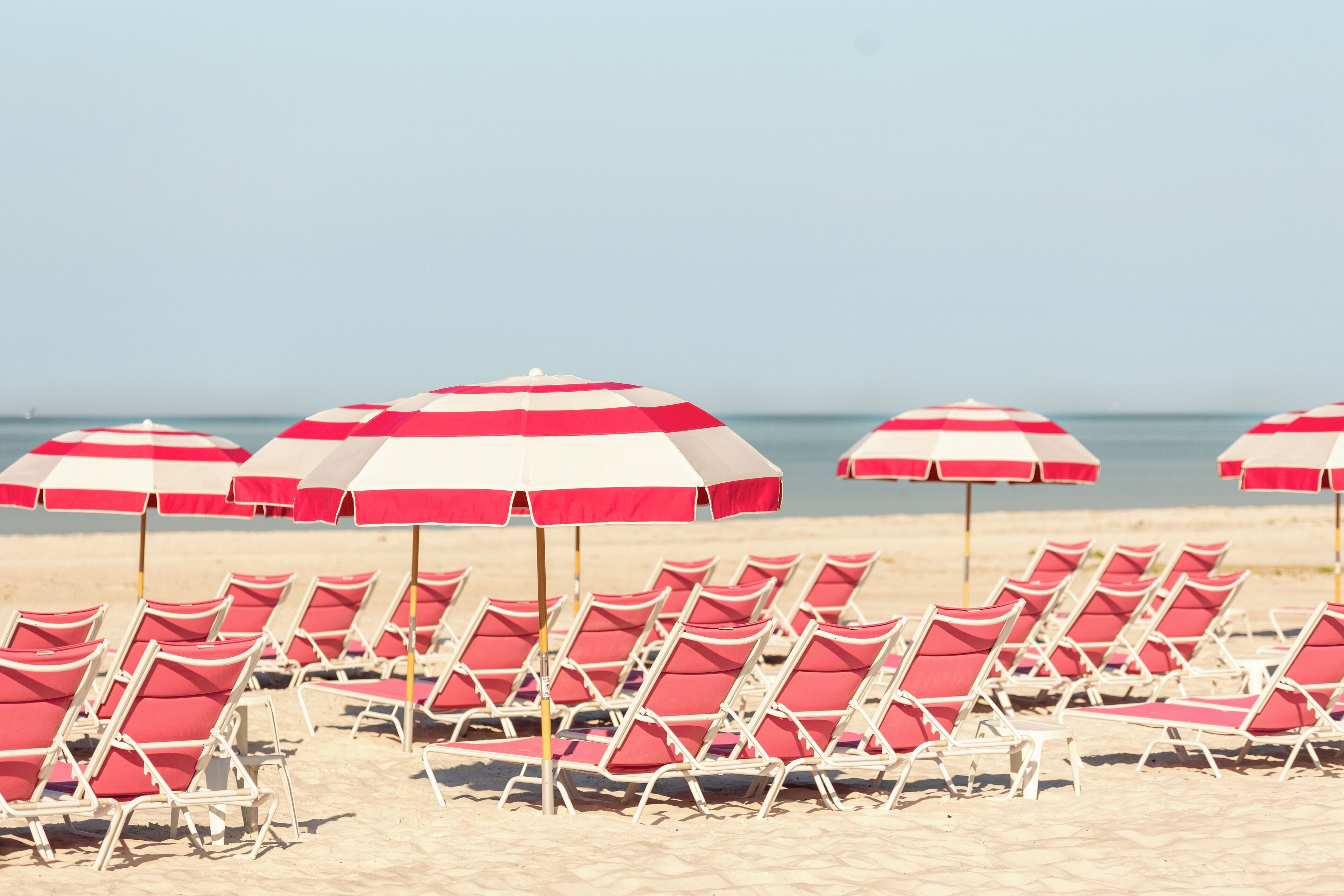 Une plage bordée de rangées de parasols de plage rayés de rouge et de blanc, accompagnés de chaises longues assorties.