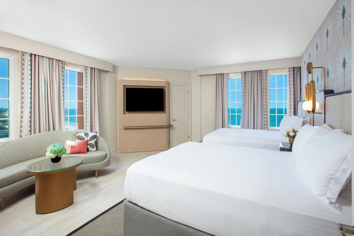 A hotel room with a sofa, two beds, a TV, and a view of the ocean.