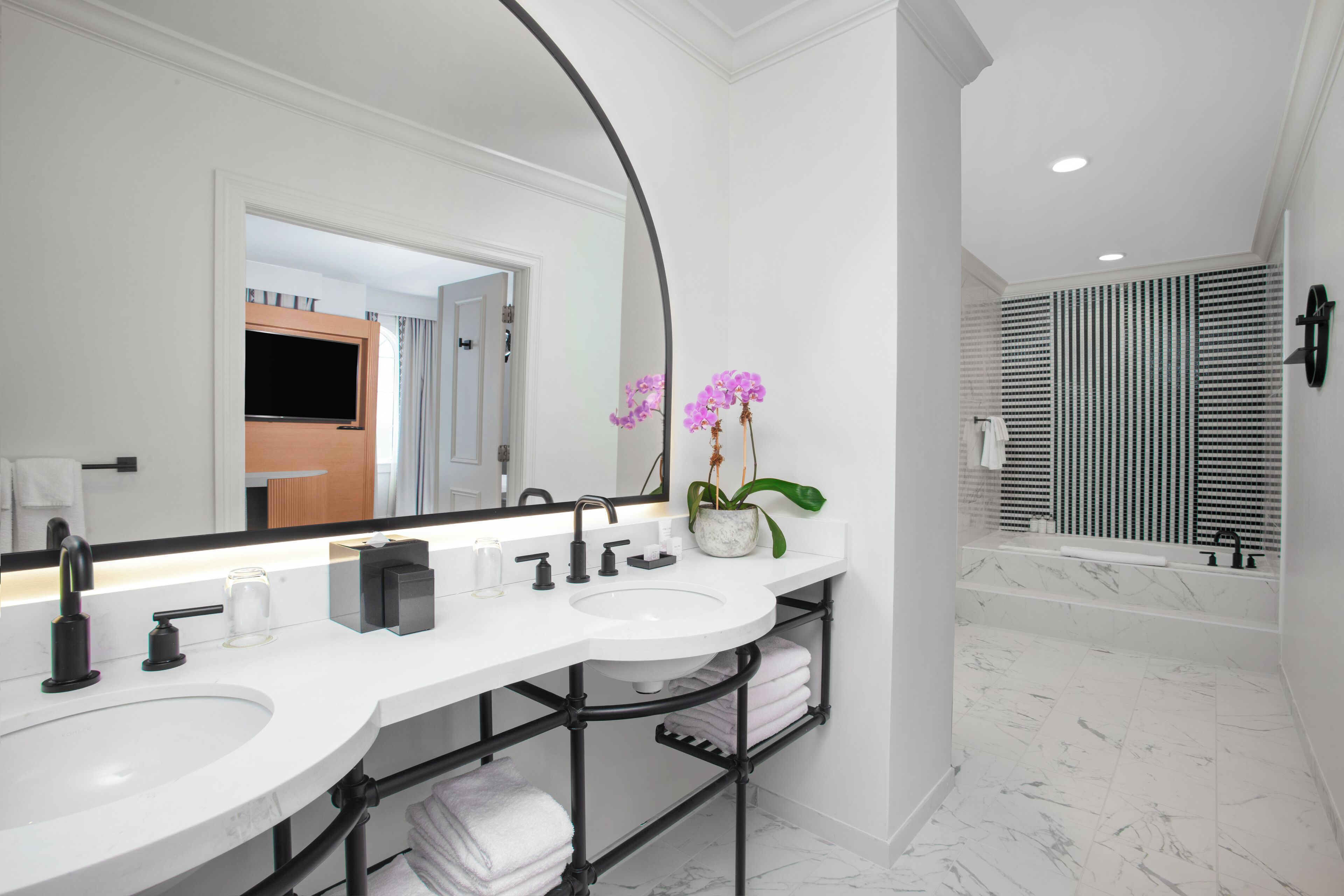 Une salle de bain moderne avec un meuble-lavabo blanc, des accessoires noirs et un grand miroir.