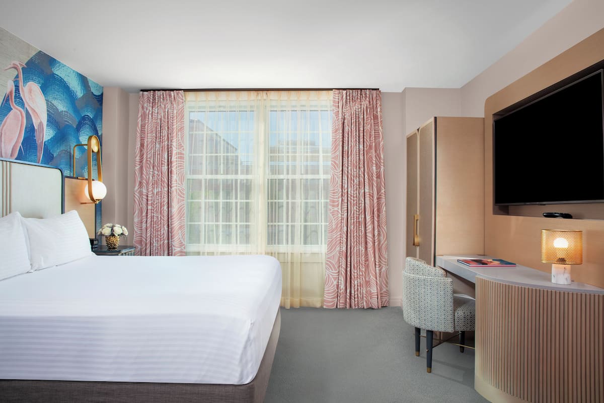 A hotel room with a bed, a desk, a chair, a TV, and a window with curtains.