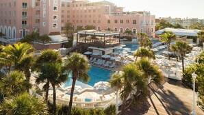 Un hotel con zona de piscina rodeada de palmeras, una terraza cubierta y múltiples sillones de descanso.