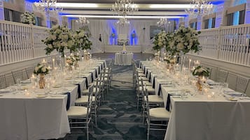 A banquet hall with rows of tables set for a wedding reception, adorned with white flowers and candles.