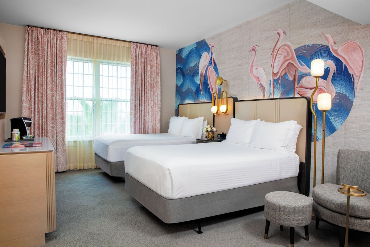 A hotel room with two beds, a desk, a chair, and a wall mural.