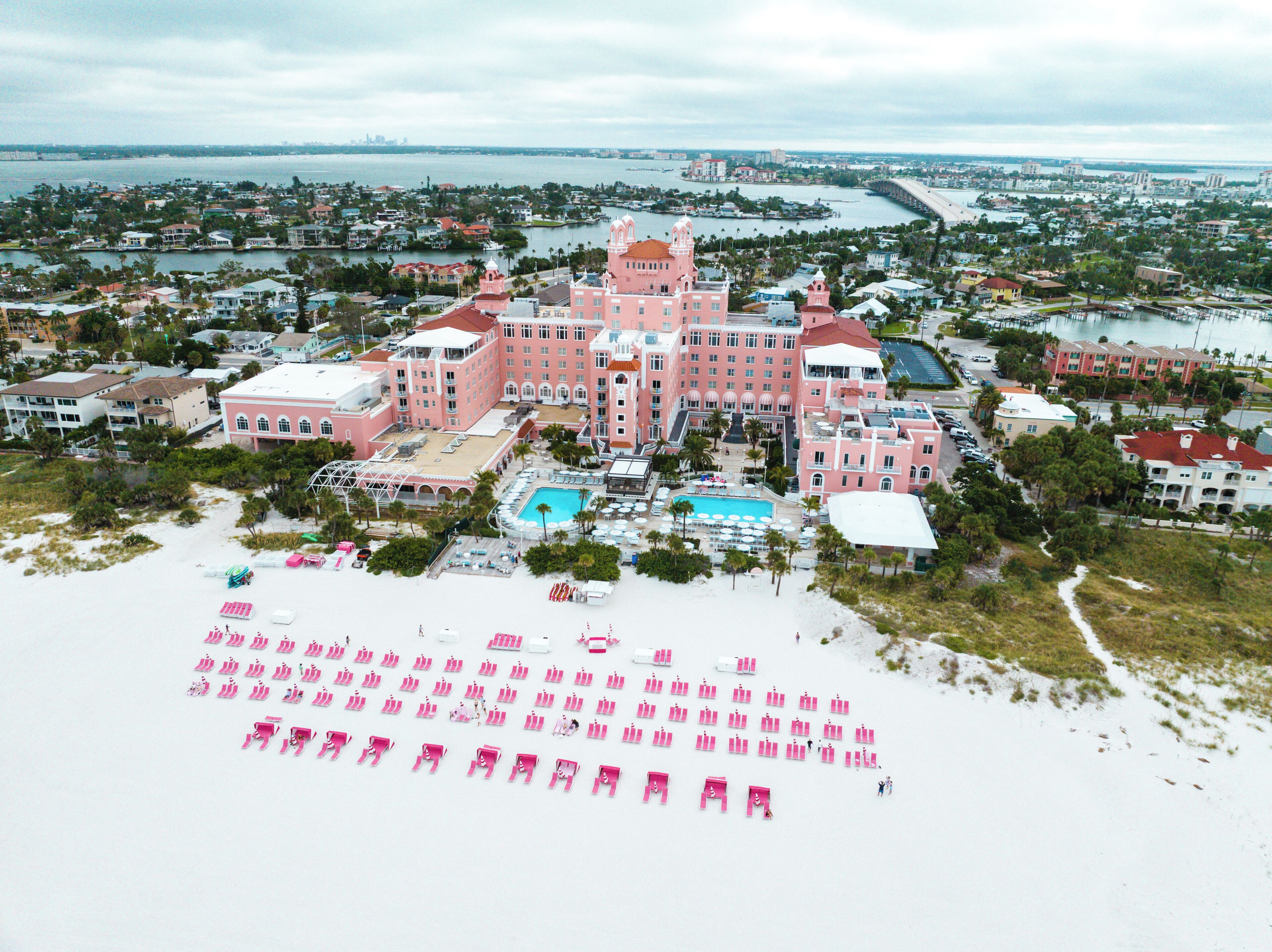 Un hotel grande de color rosa con piscina y sillas de playa sobre la arena.