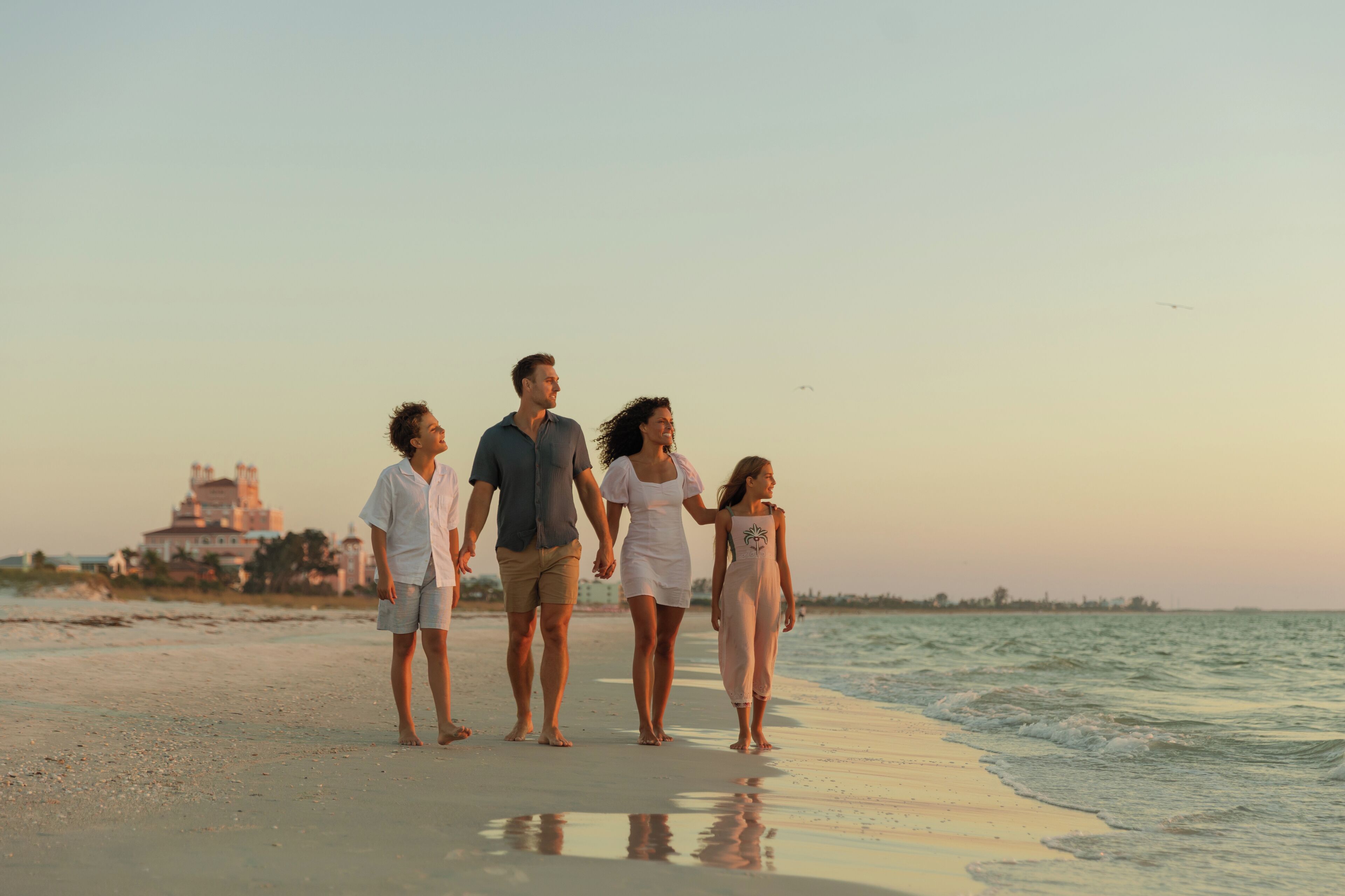 A family walking on a beach with a large building in the background.