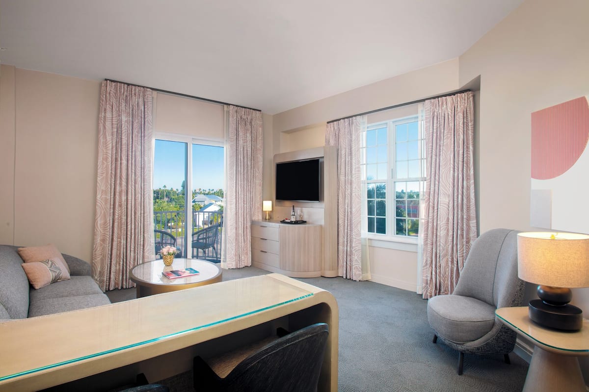 A hotel room with a sofa, a dining table, a TV, and a chair.